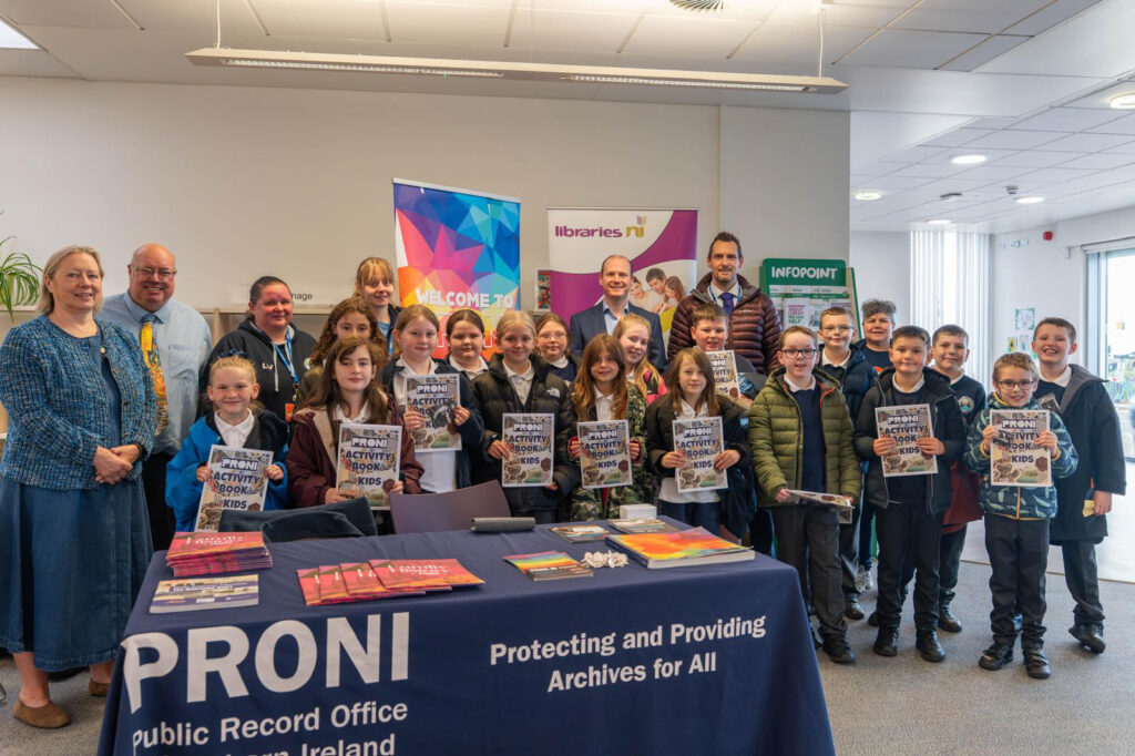 Gordon Lyons with Primary 6 pupils from Carrickfergus Integrated Primary School holding PRONI activity books at Carrickfergus Library