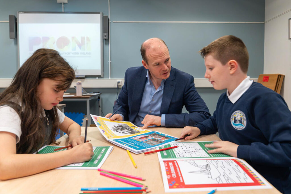 Gordon Lyons looking at the PRONI activity book with two pupils from Carrickfergus Integrated Primary School