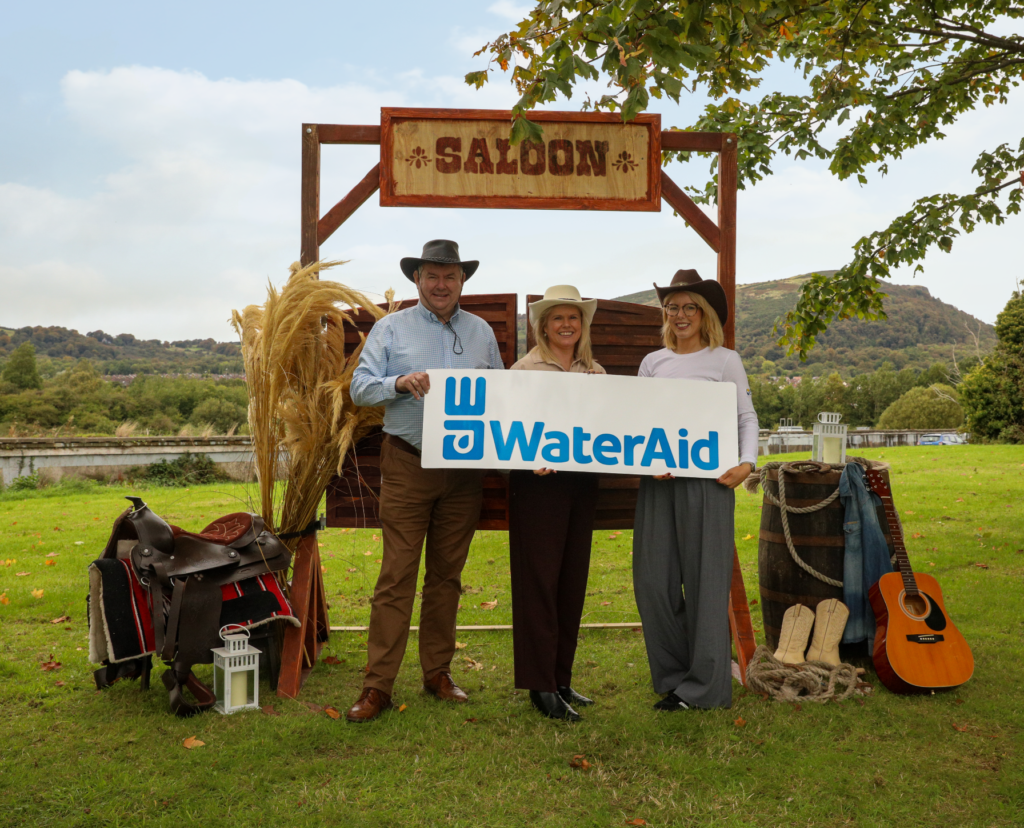 Ian Lowry, Sara Venning and Jemma Lowry wearing cowboy hats and holding a WaterAid sign to launch the fundraising ball